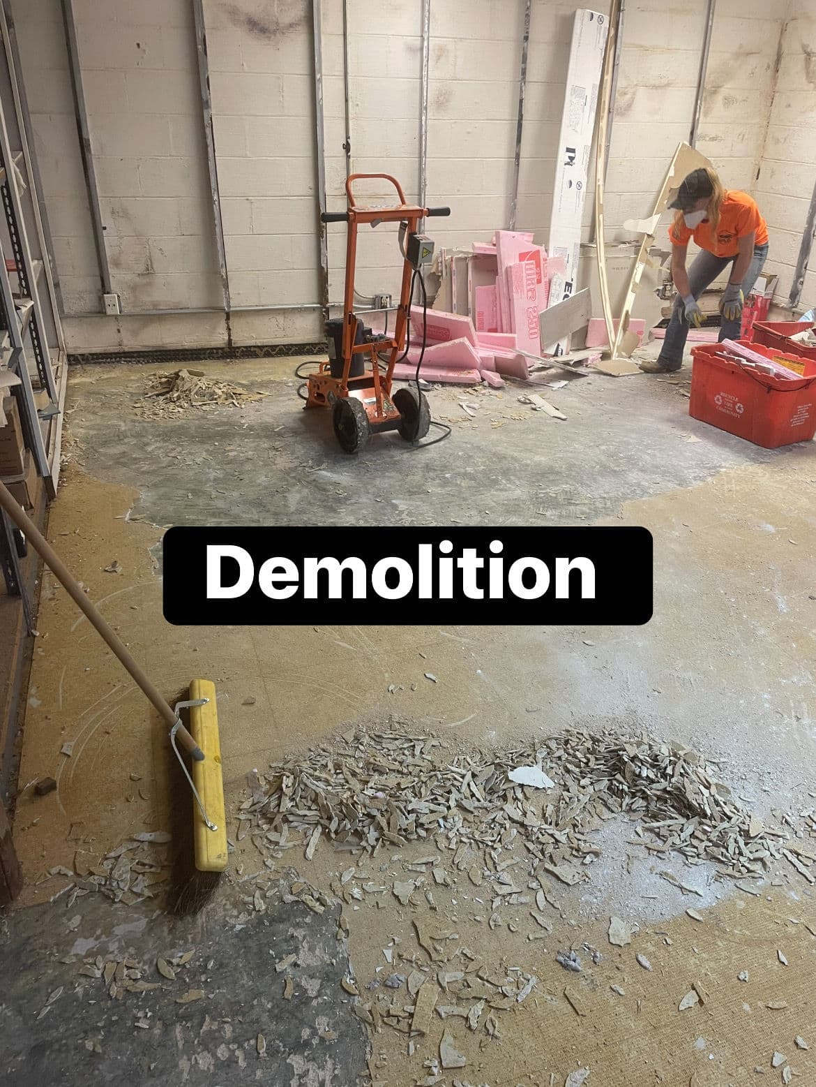 Person sweeping debris in a garage during a demolition project. Tools and materials visible.
