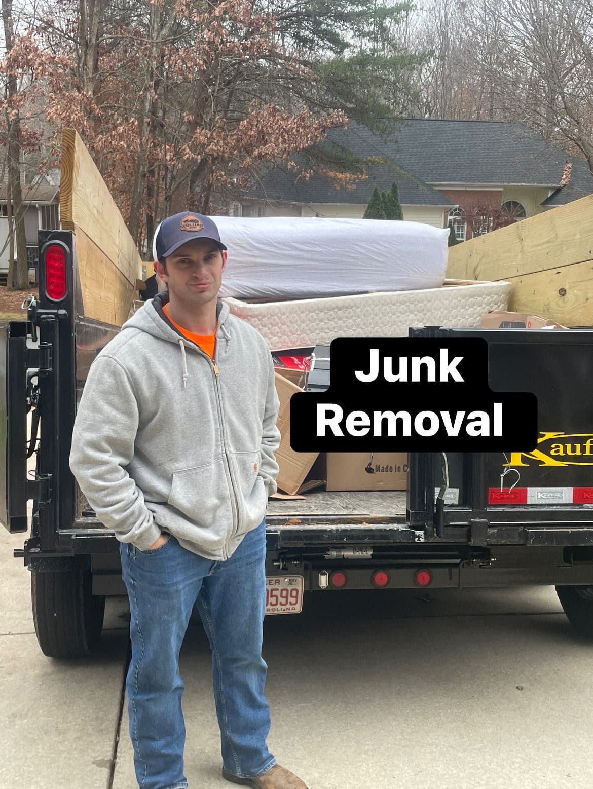 Man standing by a junk removal truck loaded with mattresses and boxes.